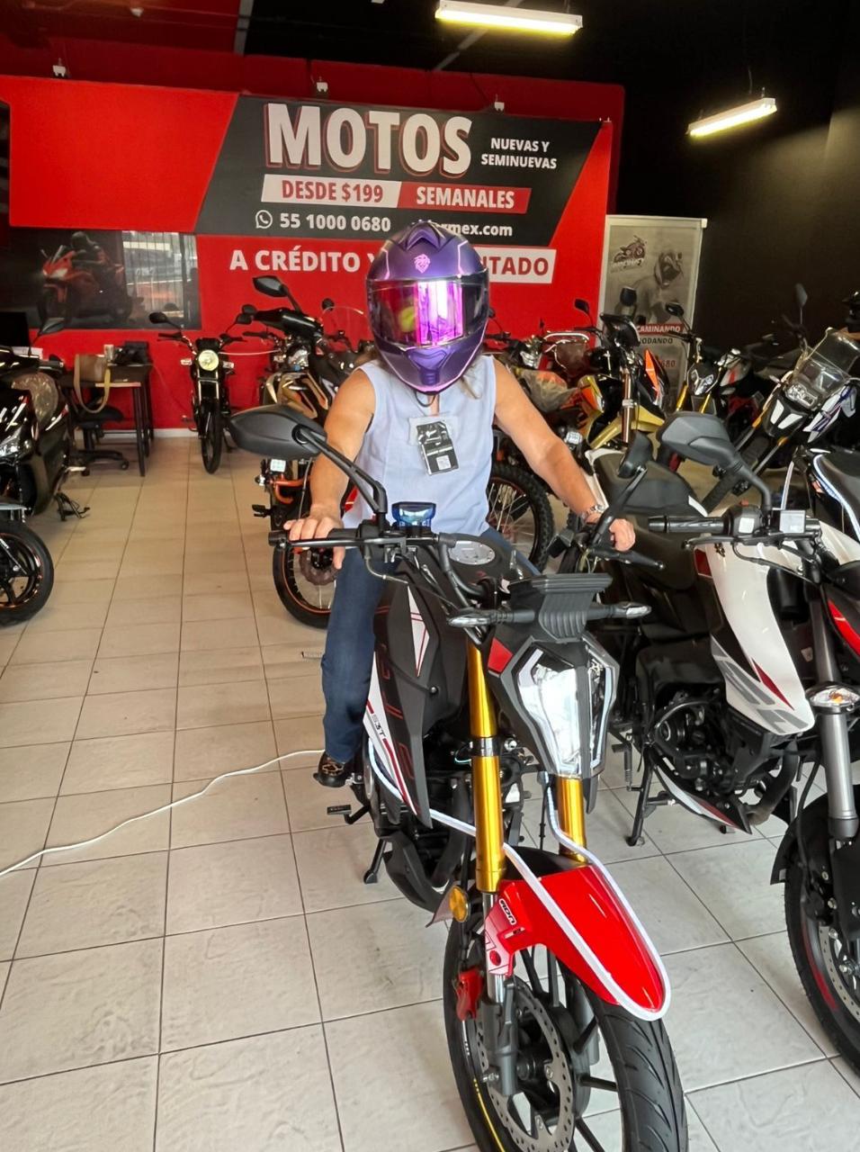 Clienta probando una motocicleta en una agencia RiderMex, con el catálogo en piso al fondo